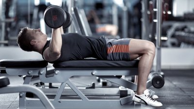 Young man doing a chest and arms workout with a dumbbell bench press exercise