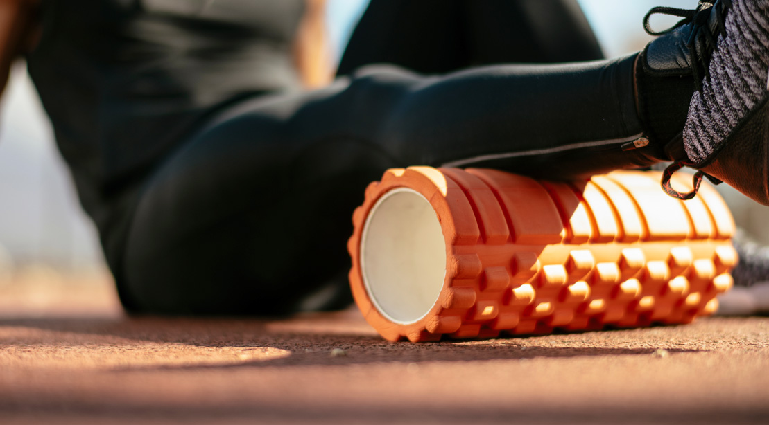 Athletic runner foam rolling his calf muscle on the track field