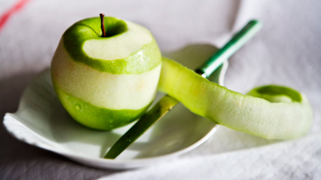 Green apple partly peeled on a plate next to a knife