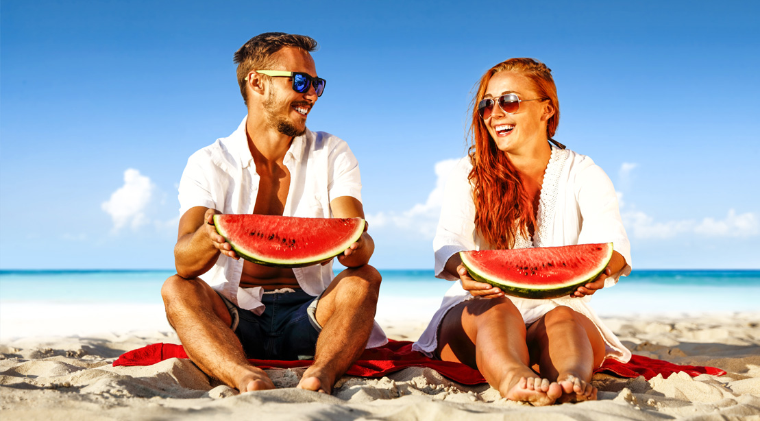 A happy fit couple eating watermelon on the beach