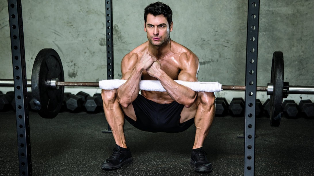 Muscular Man and fitness professional performing a Zercher Squat exercise