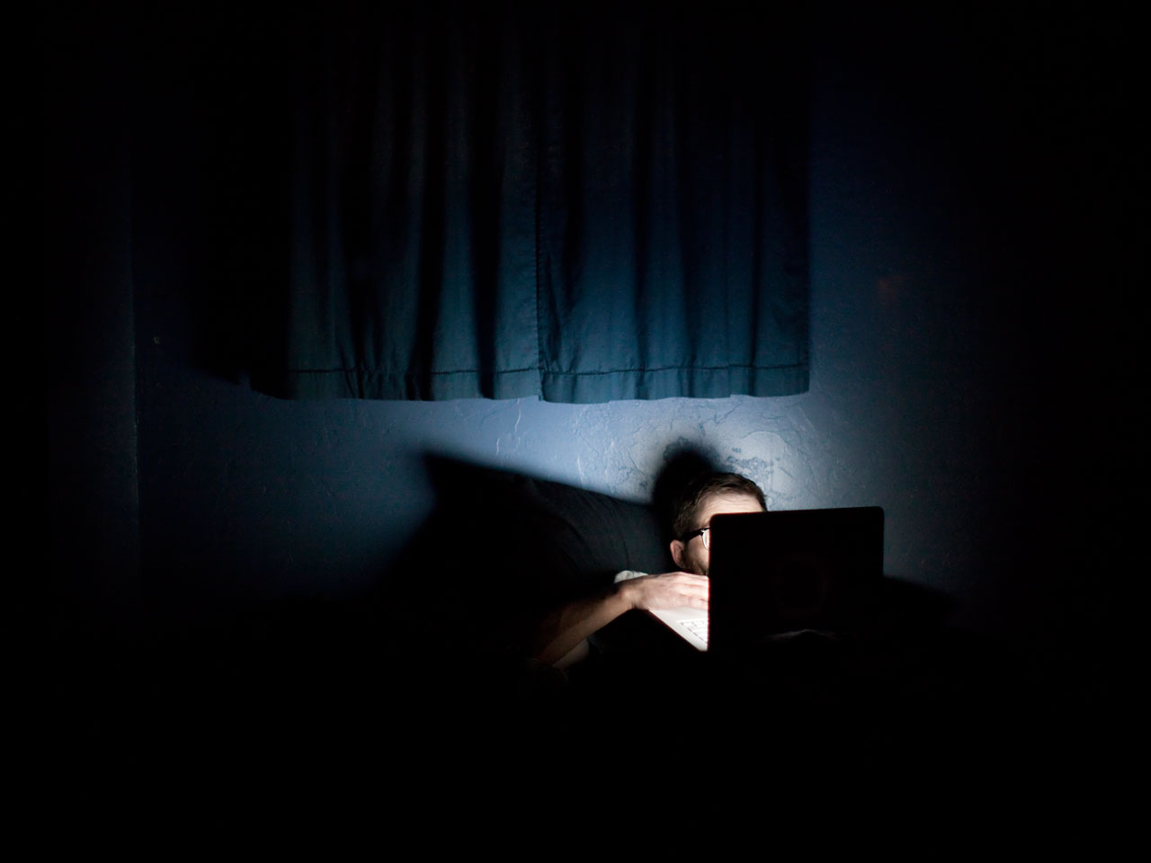 Man on laptop in bed in the dark