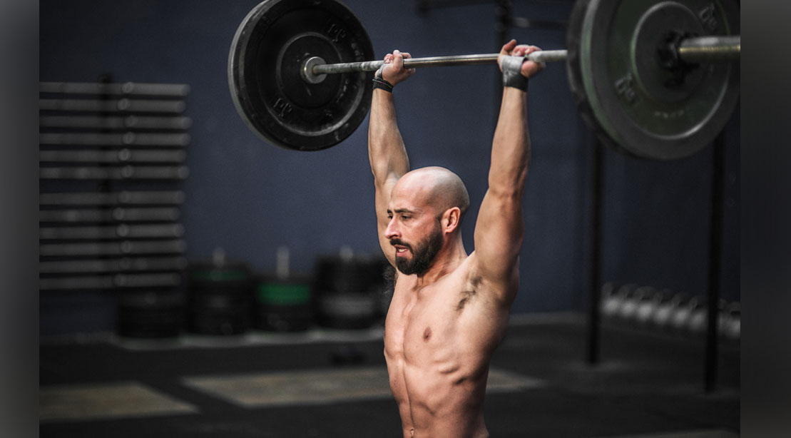 Bald fitness model performing the push press exercise for building upper and lower body muscles