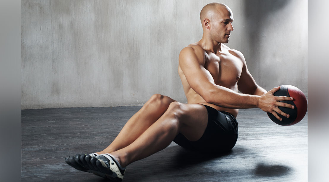 Bald fit man working out his core with a russian twist with medicine ball exercise