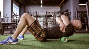 Male fitness enthusiast foam rolling exercises in an empty gym