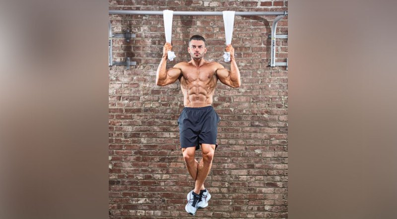 Muscular man doing forearms workout with a towel pullups exercise