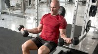 Fit bald man doing arm workouts with a incline dumbbell curl exercise