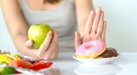 Female eating an apple while pushing away a plate of unhealthy foods.