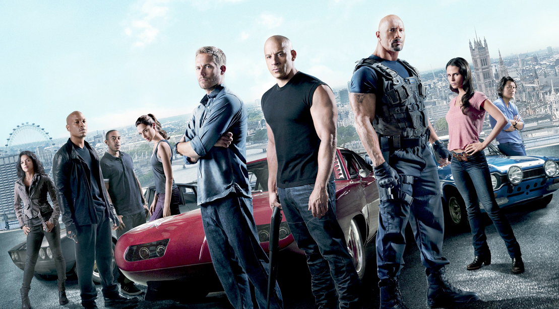 Gal Gadot Paul Walker Vin Diesel and The Rock Standing In Front of Customized Cars For Fast and Furious Movie