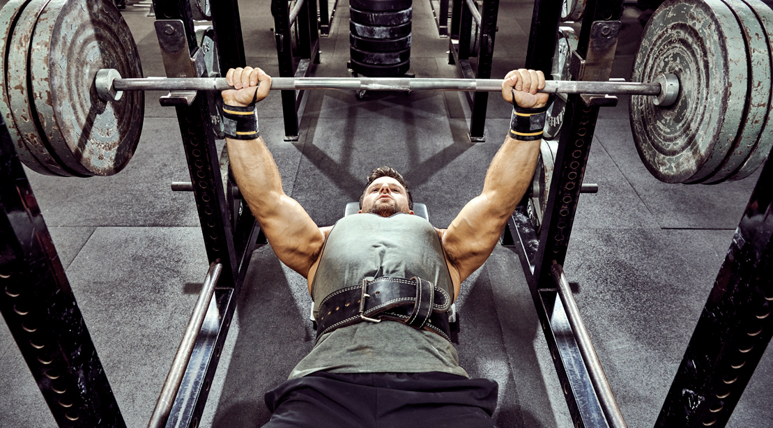 Bodybuilder and muscular man working out his upper muscles with a barbell bench press