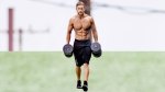 Male fitness model with a muscular core doing forearm workouts with dumbbell farmer's carry exercise
