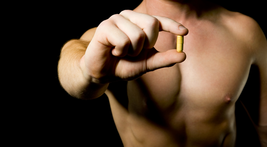 Muscular man holding a pill