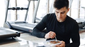 Man wearing black eating a pre-workout meal prepped food in front of treadmills
