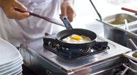 Chef cooking eggs sunny side up in a small frying pan