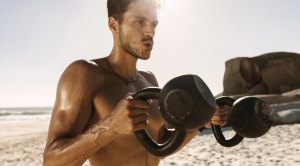 Man working out on the beach with kettlebells performing a KB workout