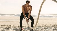 Fit man working out on the beach using battle ropes