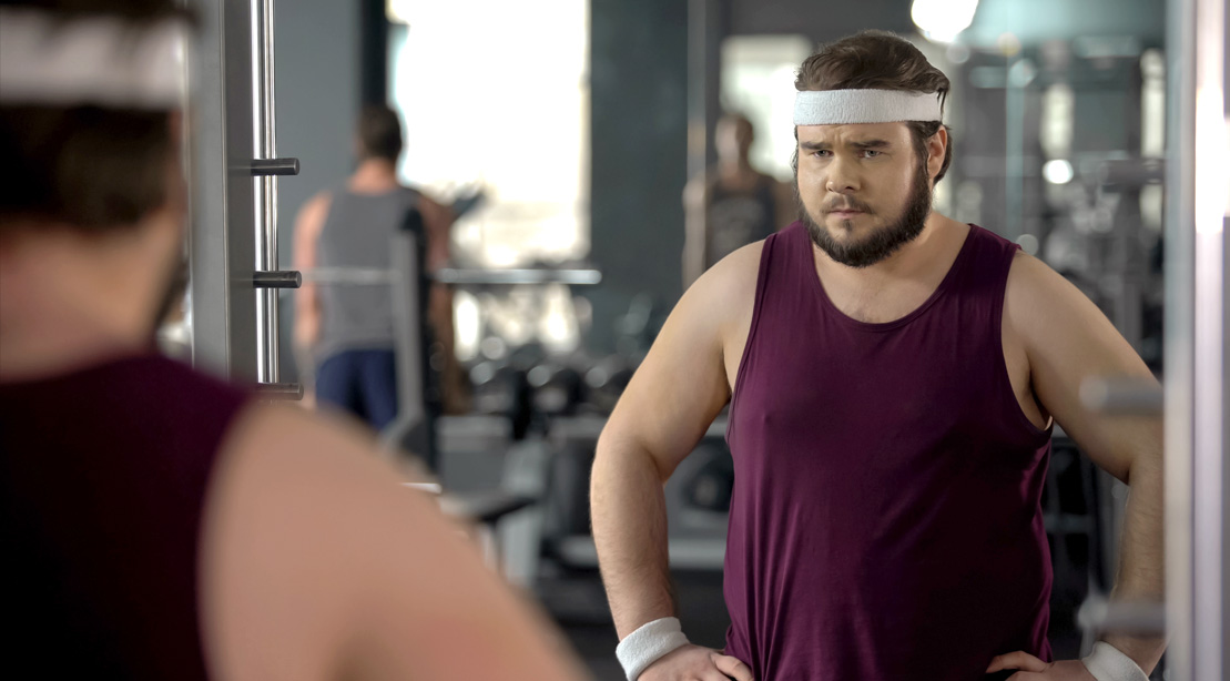 overweight man looking into the mirror in the gym