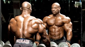 Bodybuilder Dexter Jackson looking in the mirror by the dumbbell rack