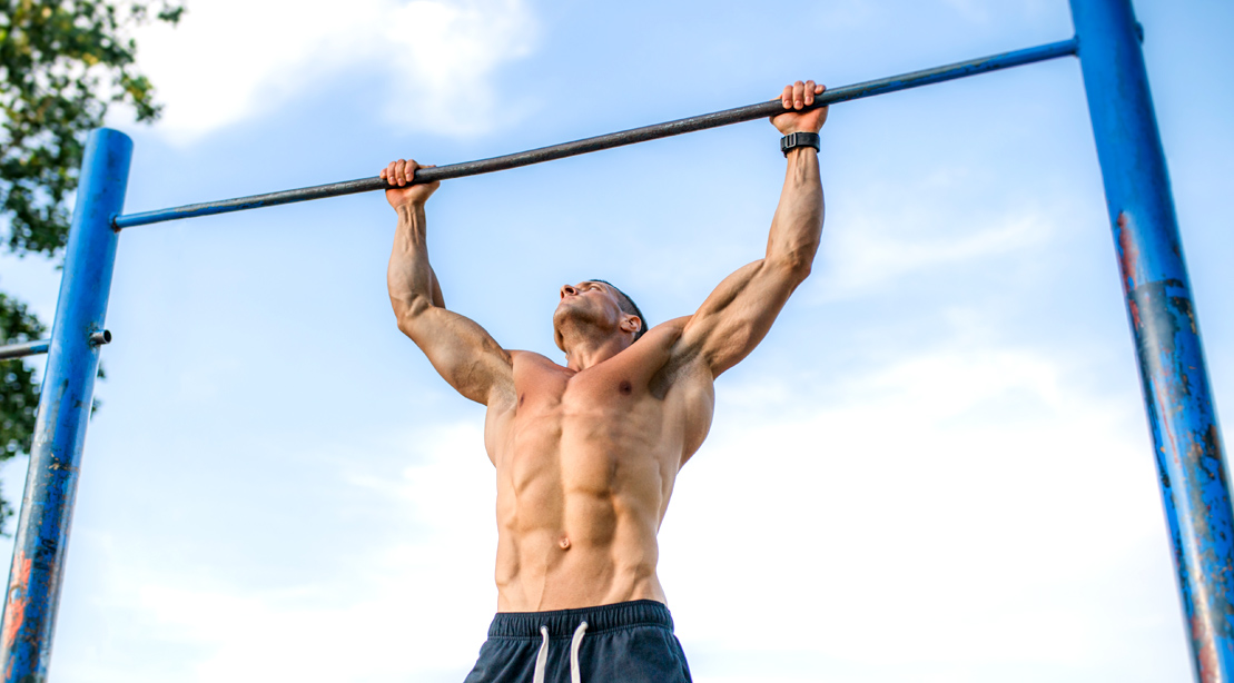 Man working out outdoors doing pull up exercise in the park on a nice blue sky day