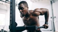 Muscular black man working out his arms and back by doing dip exercise