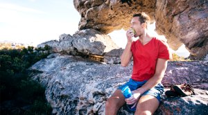 Aging man experiencing metabolism slows down eating an apple on a mountain after a hike