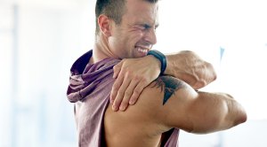 Fit muscular man suffering from muscle soreness in his shoulder