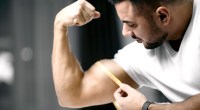 Strong muscular man measuring his bicep growth using a measuring tape