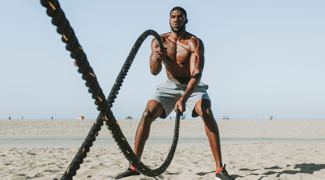 Muscular man working out with battle rope exercises on the beach