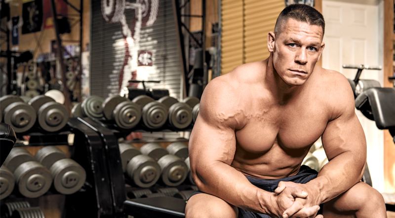 WWE Wrestler and movie star John Cena sitting and resting on a bench in a gym with his shirt off showing off his muscular hollywood physique