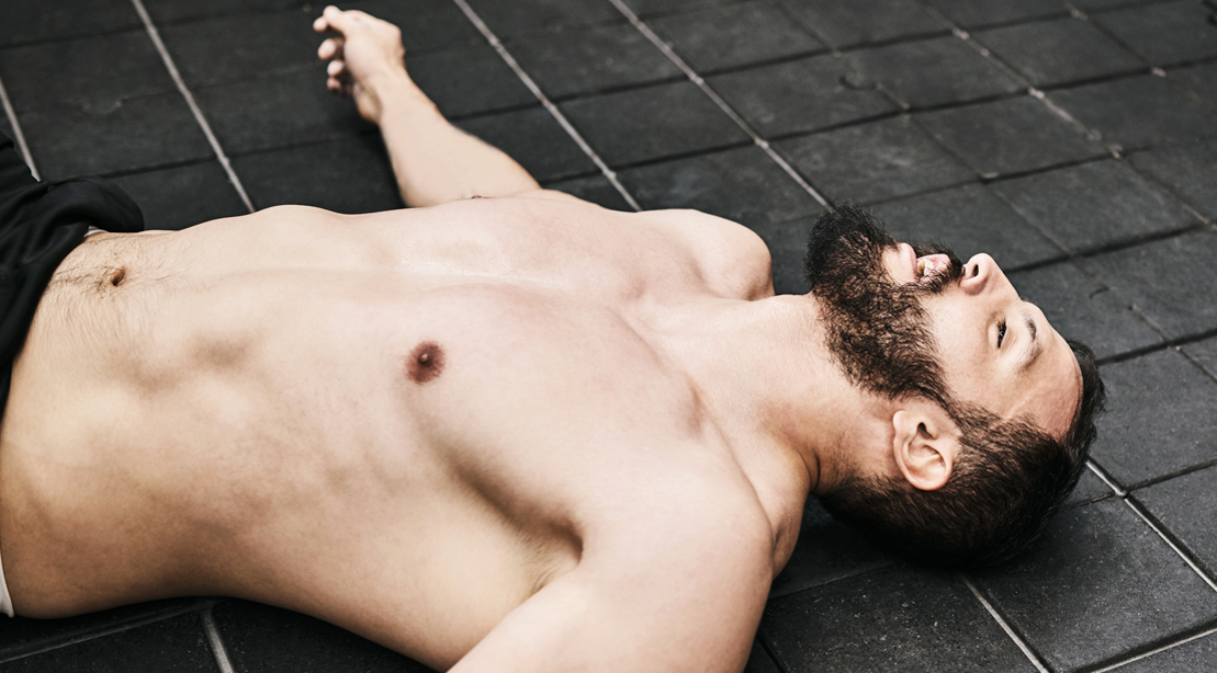 muscular topless bodybuilder laying on the floor of a gym