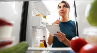 Girl with a notebook writing her a spring clean grocery list while looking in her fridge