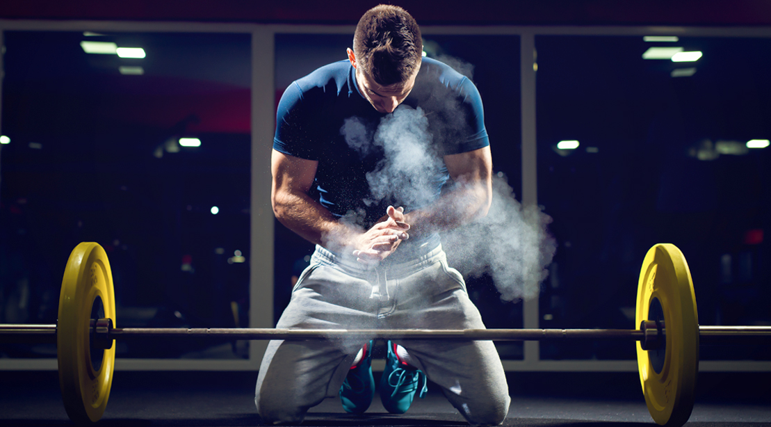 Man preparing to lift a heavy barbell using chalk for a high-level athletic workout program