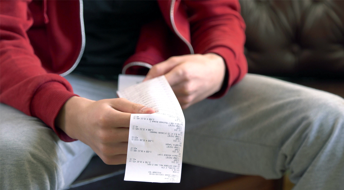 Person-Looking-At-Shopping-Receipt-On-Couch