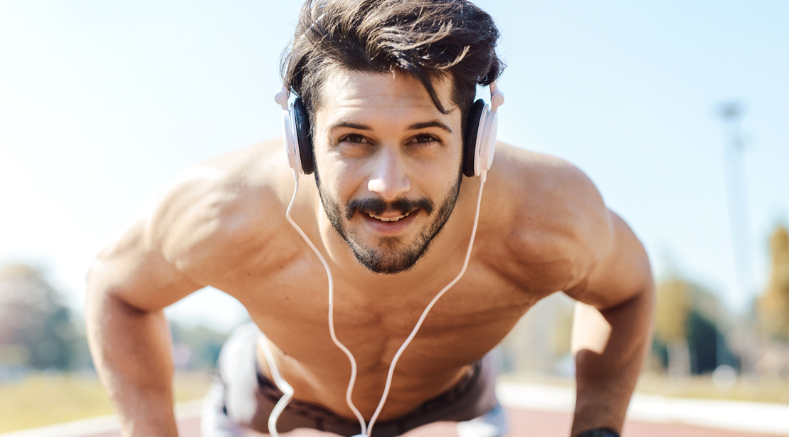 Physically fit man wearing headphones while doing outdoor exercises