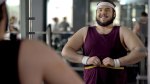 Happy and overweight man who lost weight from his fitness resolution measuring his stomach in the gym mirror