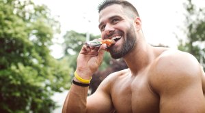 Happy bodybuilder eating a pre-workout protein bar outdoors