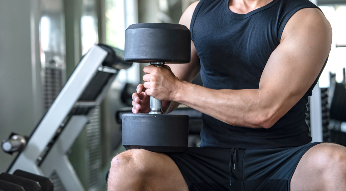 Muscular man with biceps holding a heavy dumbbell sitting on his knee