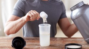 Muscular fit man adding whey protein powder into a shaker