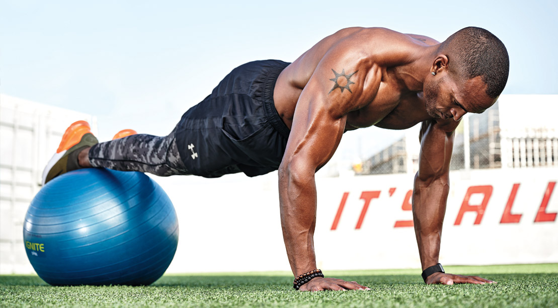 Man training outdoors doing plank with feet on ball