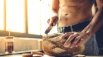 Muscular man cutting a loaf of fresh baked bread in his kitchen with a bread knife