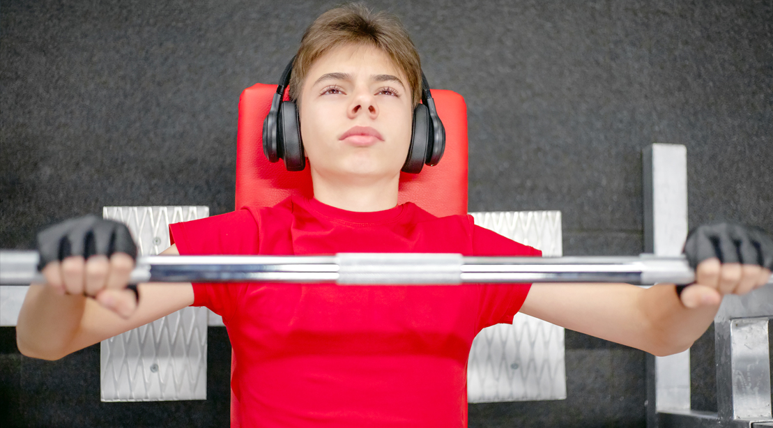 Young-Adult-Teen-Wearing-Headphones-Lifting-Barbell-Bench-Press