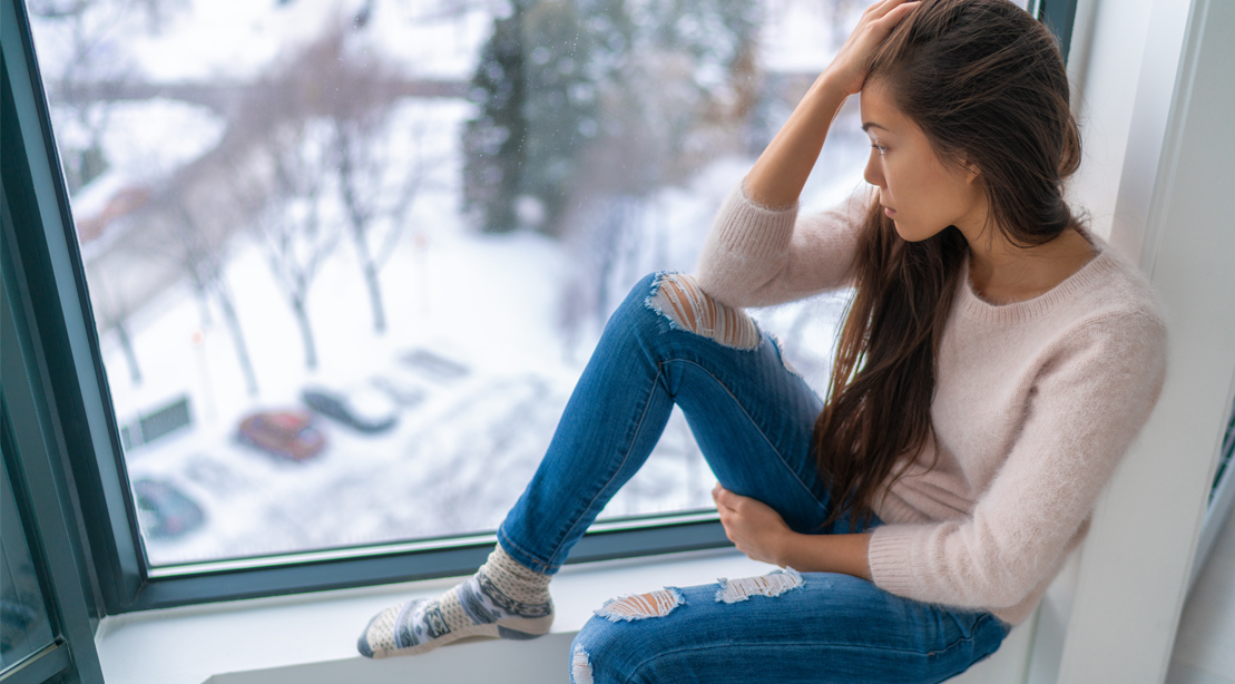 Asian-Girl-Sitting-On-Window-Ledge-Looking-Out-Winter-Depressed-Sad-Mental-Health