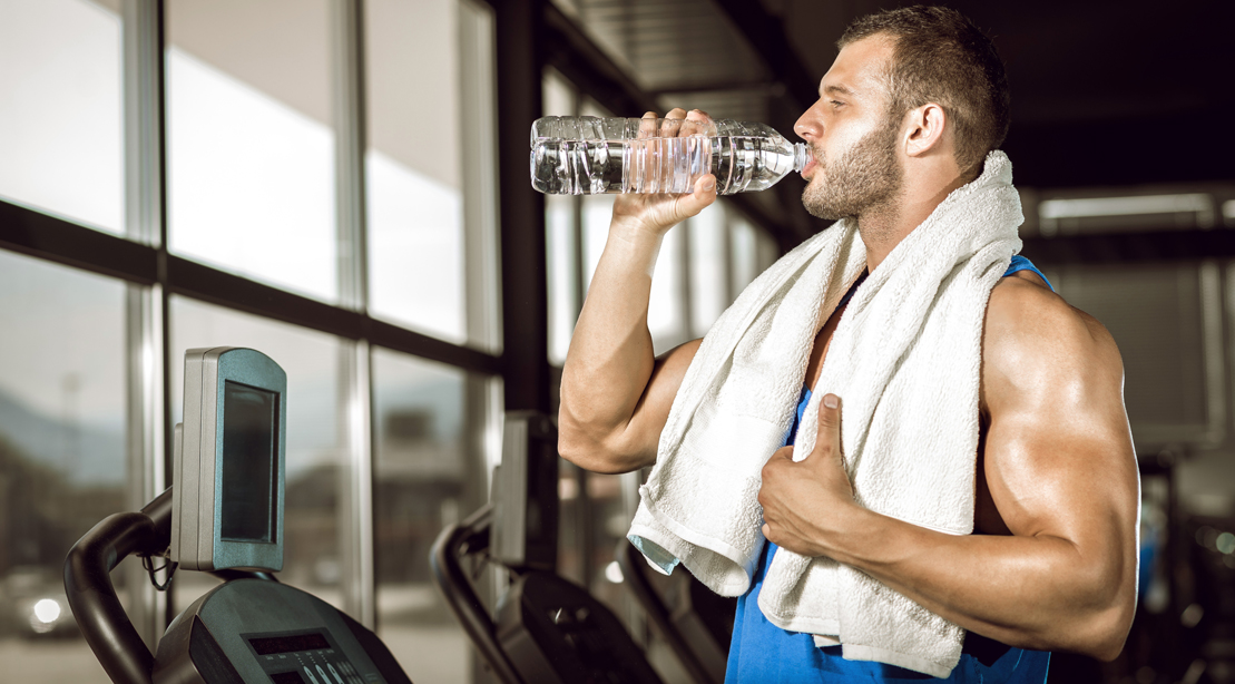 Sweaty man drinking a bottle of water after a workout in the gym