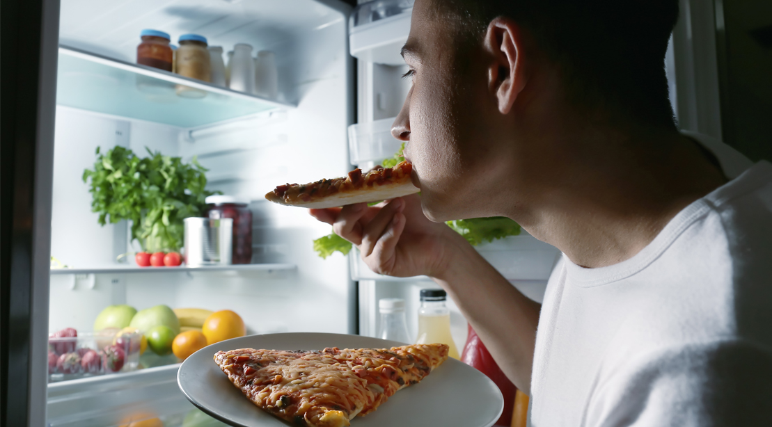 Man-Eating-Pizza-In-Front-Of-Refrigerator