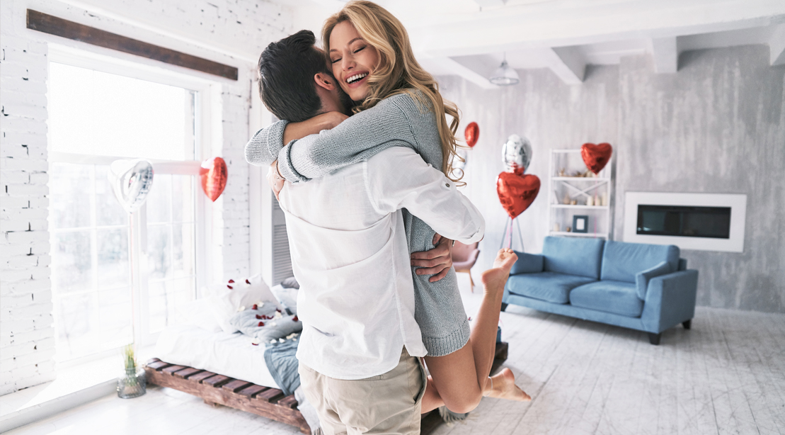 Female-Hugging-Male-Romantic-Couple-Valentines-Day-Heart-Shaped-Balloons-Filled-Room