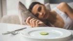 Thin malnurished female staring at a plate with a single slice of cucumber while laying on the couch