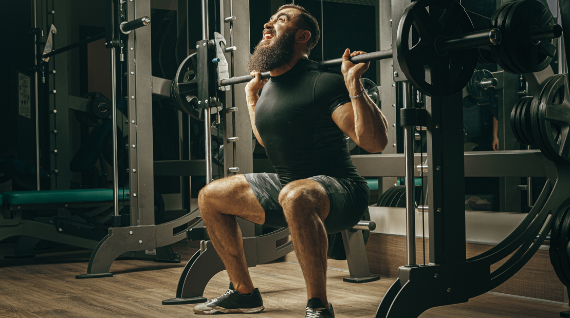 Bearded weight lifter struggling with a squat at smith machine and performing squat accessory exercises