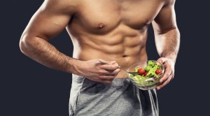 Muscular man with shredded abs eating a salad bowl