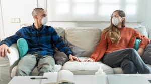 Couple social distancing and wearing face mask in the living room couch during covid-19 pandemic