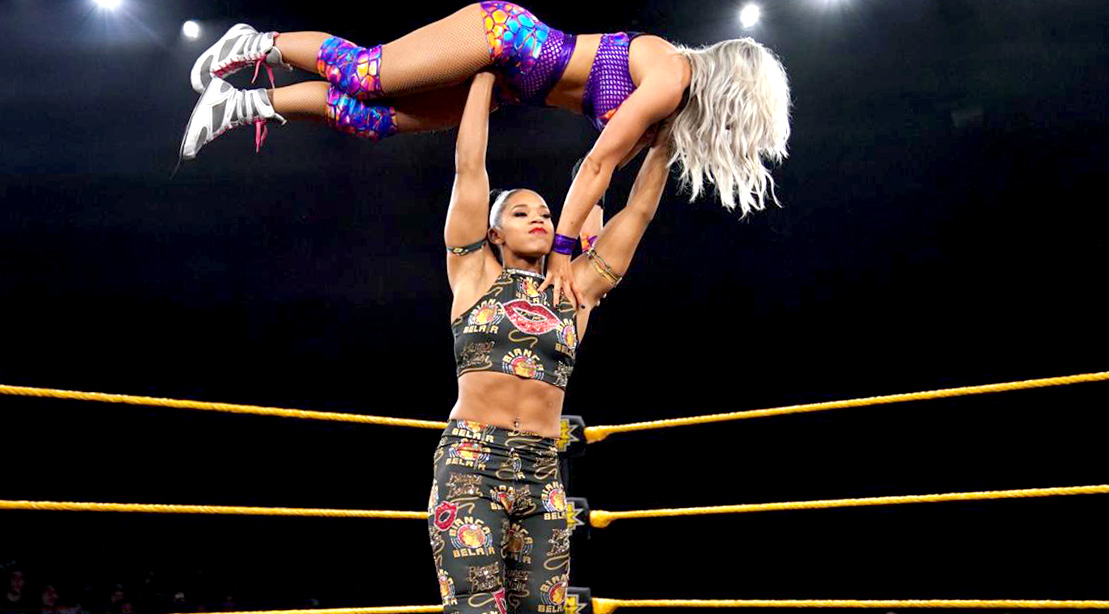 WWE pro-wrestler Bianca Belair performing overhead press with another wrestler